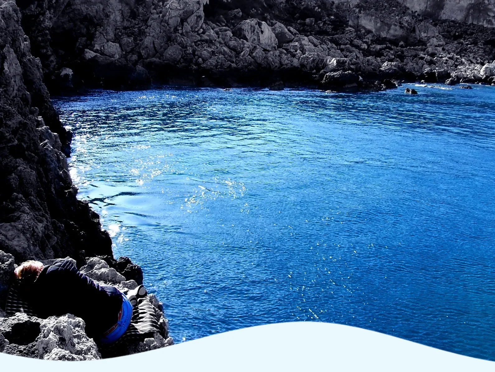 Clear blue water surrounded by rocky cliffs under a bright sky.